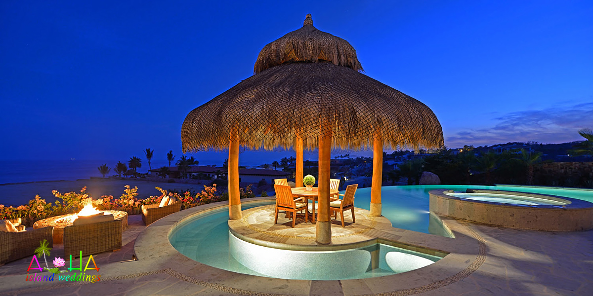 Thatched cabana and pool lit up at dusk at the oceanfront estate